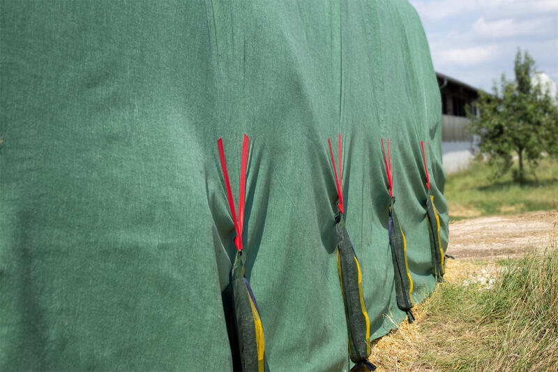 4 grüne Silosäcke mit rotem Klettband FixTex an grünem Vlies befestigt und hängend